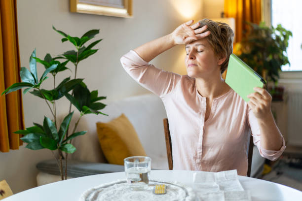A woman is trying to cool down during a hot menopausal flash, sitting at a dining table at home