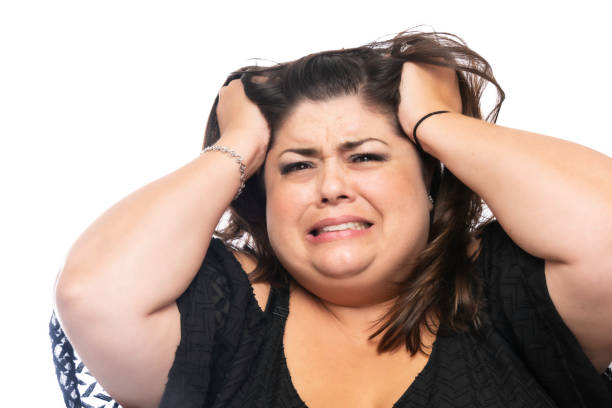 Desperate Overweight Mid adult woman looking at the camera with her hands holding her hair on white background